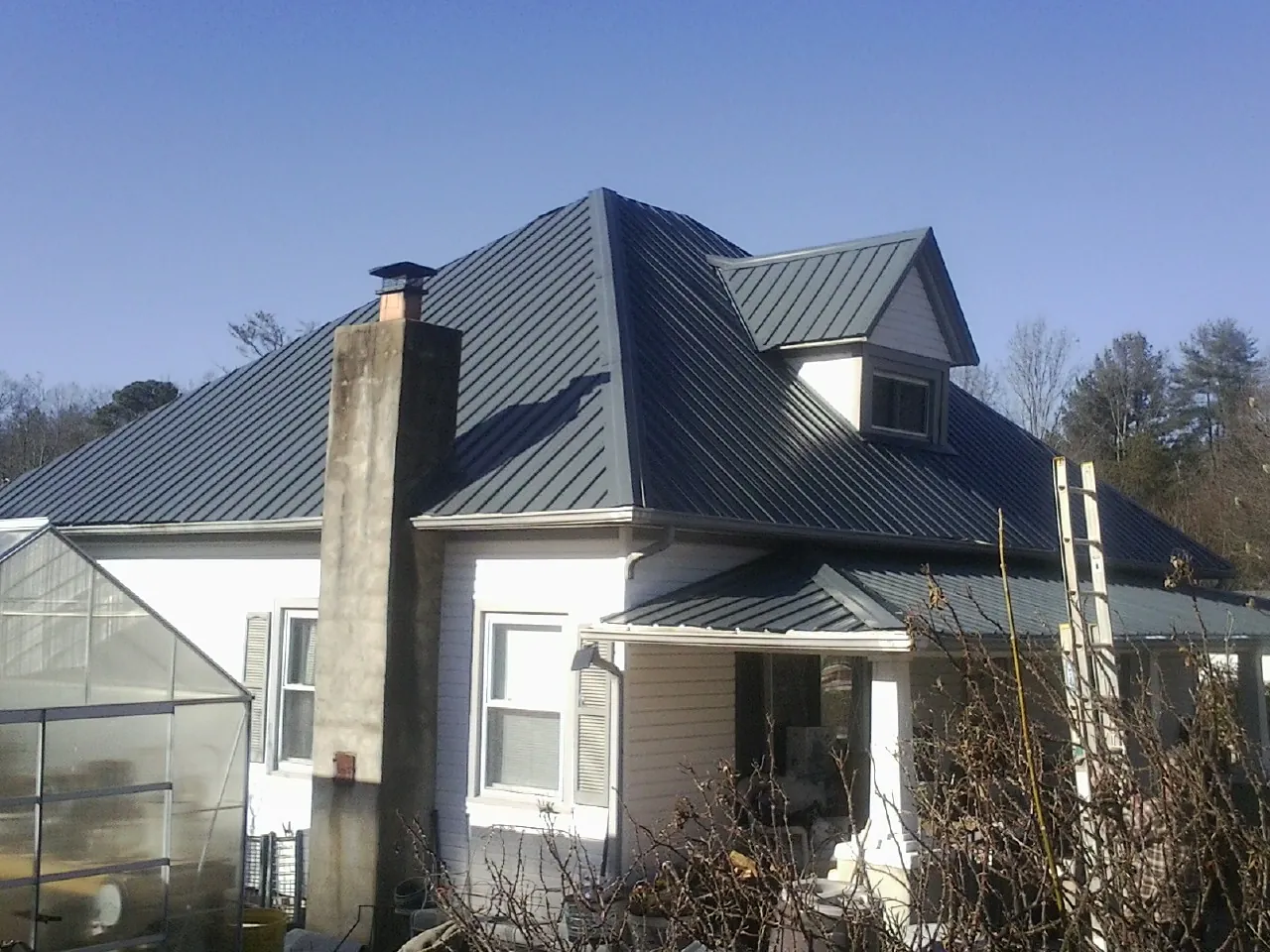 Dark blue standing seam metal roof on a white farmhouse with dormer — Slate & Tile Roof Repair by Roofing Brothers in Zionsville