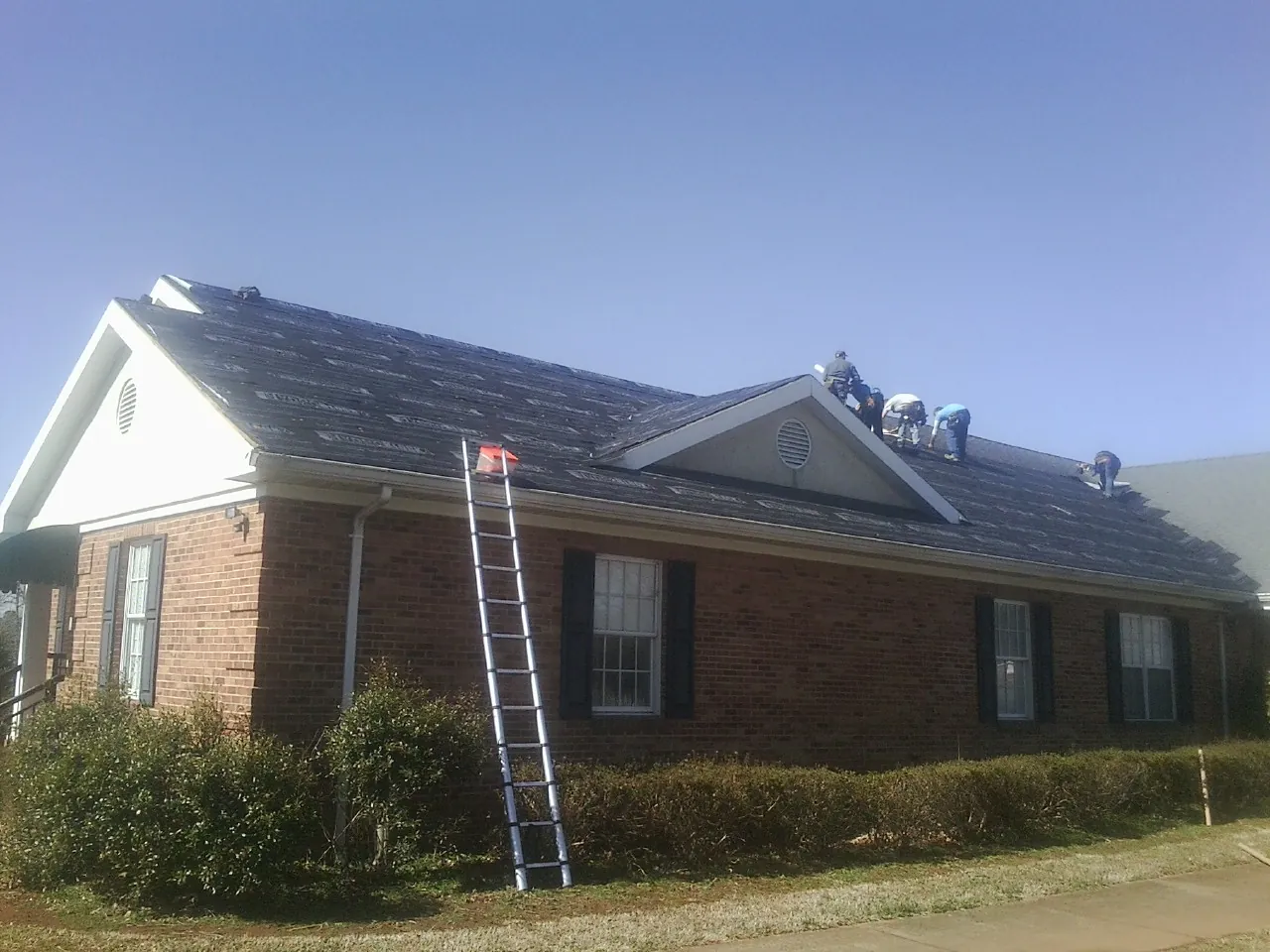 Crew tearing shingles off a brick ranch roof with a ladder set — Metal Roof Repair work by our crew in Zionsville