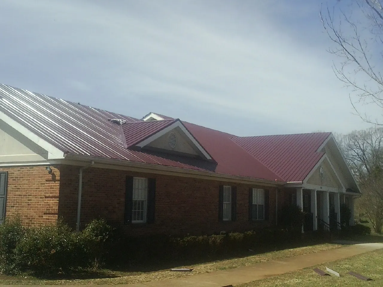 Red metal roof with gabled entries on a long brick building, from a Hail Damage Roof Repair job in Zionsville